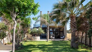 A modern house with a well-maintained lawn, palm trees, and a patio area with outdoor furniture. - Evdokia Beach Resort (Malevizi)