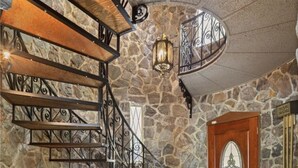 Una escalera de paredes de piedra con barandillas metálicas y una puerta de madera con un panel de vidrio decorativo.