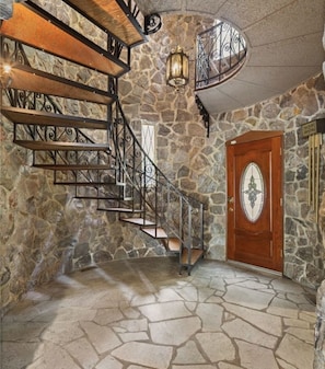 Eine Treppe mit Steinwänden, Metallgeländern und einer Holztür mit dekorativem Glasfenster.