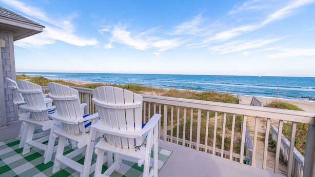 Ein Balkon mit weißen Adirondack-Stühlen, der auf einen Strand blickt.