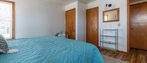A bedroom with a bed, a chair, a wardrobe, a mirror, and a shelf.