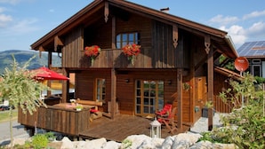 Un chalet de madera con balcón, mobiliario exterior y vistas a las montañas.