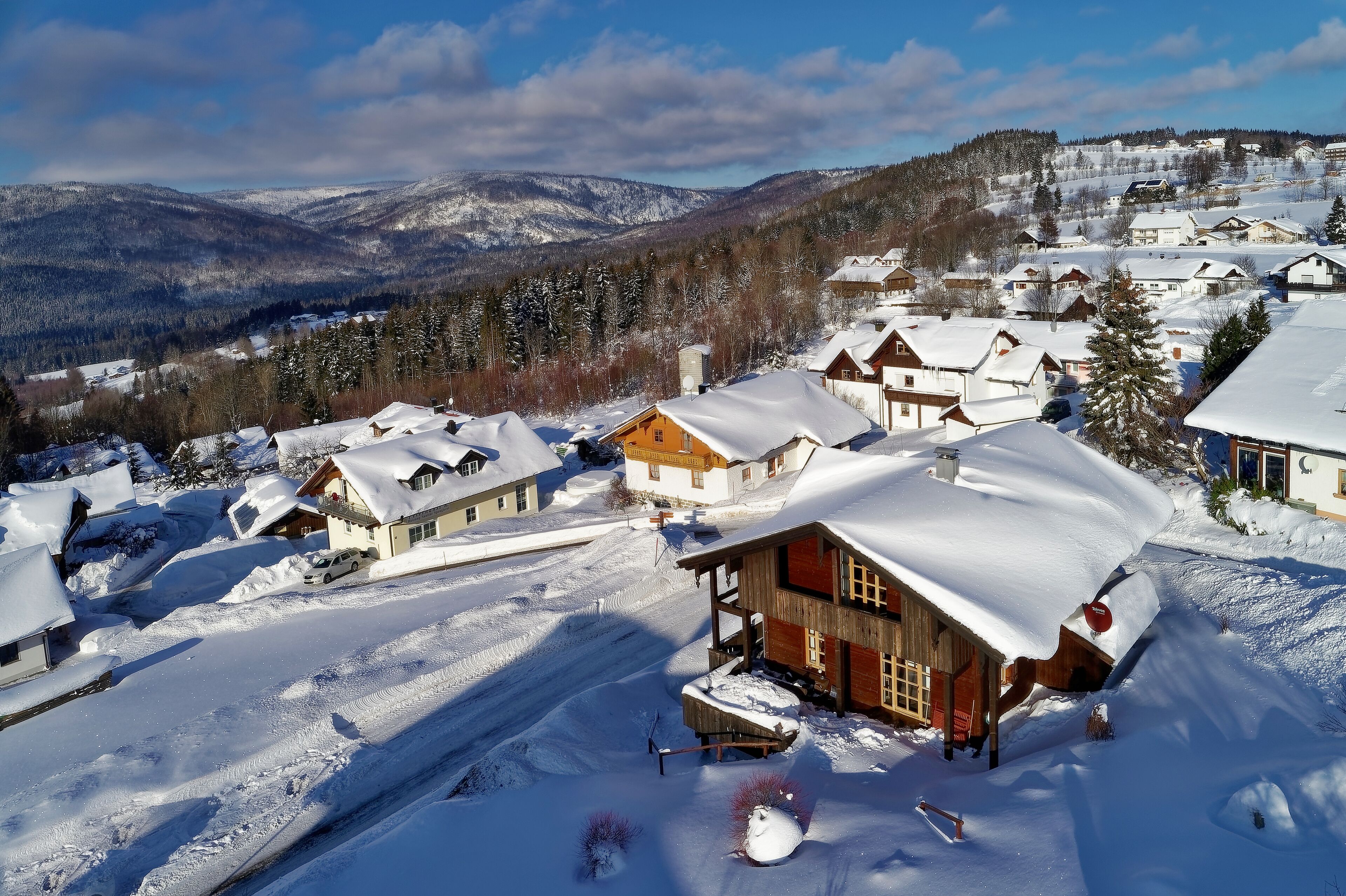 Un village enneigé, avec des maisons en bois, un télésiège et une chaîne de montagnes en arrière-plan.