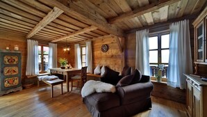 Interior acogedor de una cabaña con techo de madera, un sofá, una mesa de comedor y una ventana con cortinas.