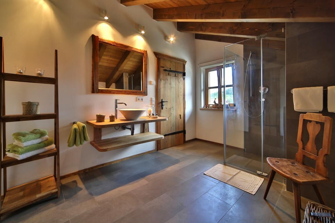 Une salle de bain avec un meuble-lavabo en bois, un grand miroir, une douche en verre et une chaise en bois.