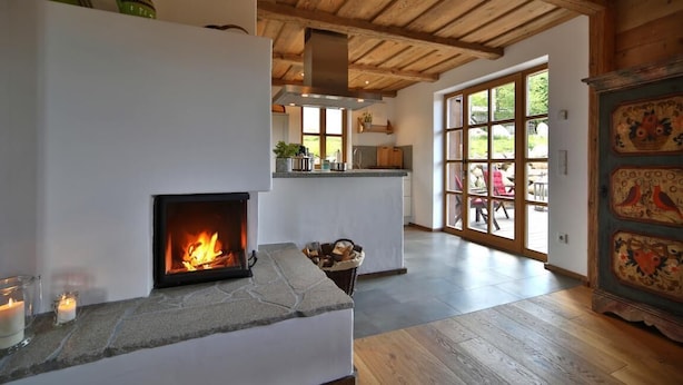 Un interior acogedor con chimenea, techo de madera y vistas a un área exterior a través de un ventanal.