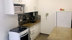 Uma cozinha compacta com armários brancos, micro-ondas, fogão e pia.