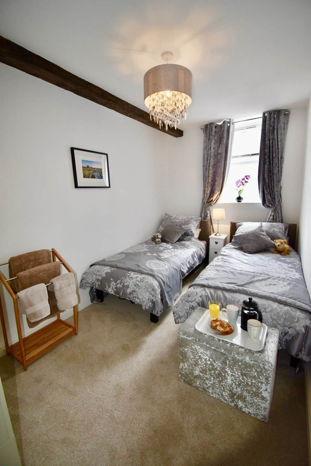 Een slaapkamer met twee bedden, een houten stoel, een klein tafeltje met ontbijtartikelen en een kroonluchter.