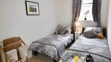 Een slaapkamer met twee bedden, een houten stoel, een klein tafeltje met ontbijtartikelen en een kroonluchter.