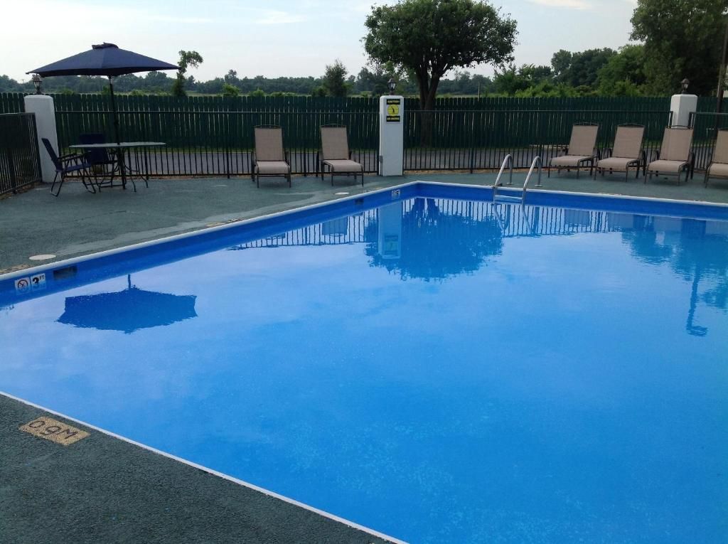 A rectangular swimming pool with a clear blue surface, surrounded by a fence, and a few lounge chairs and an umbrella.