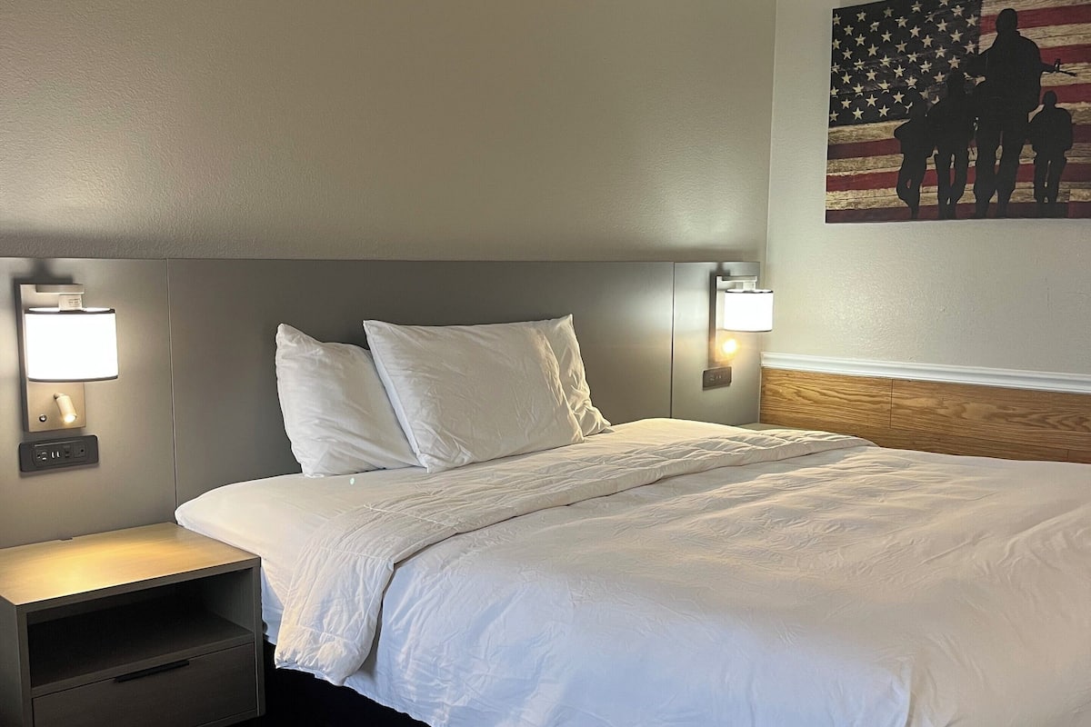 A neatly made bed with white linens, a wooden headboard, and two bedside lamps.