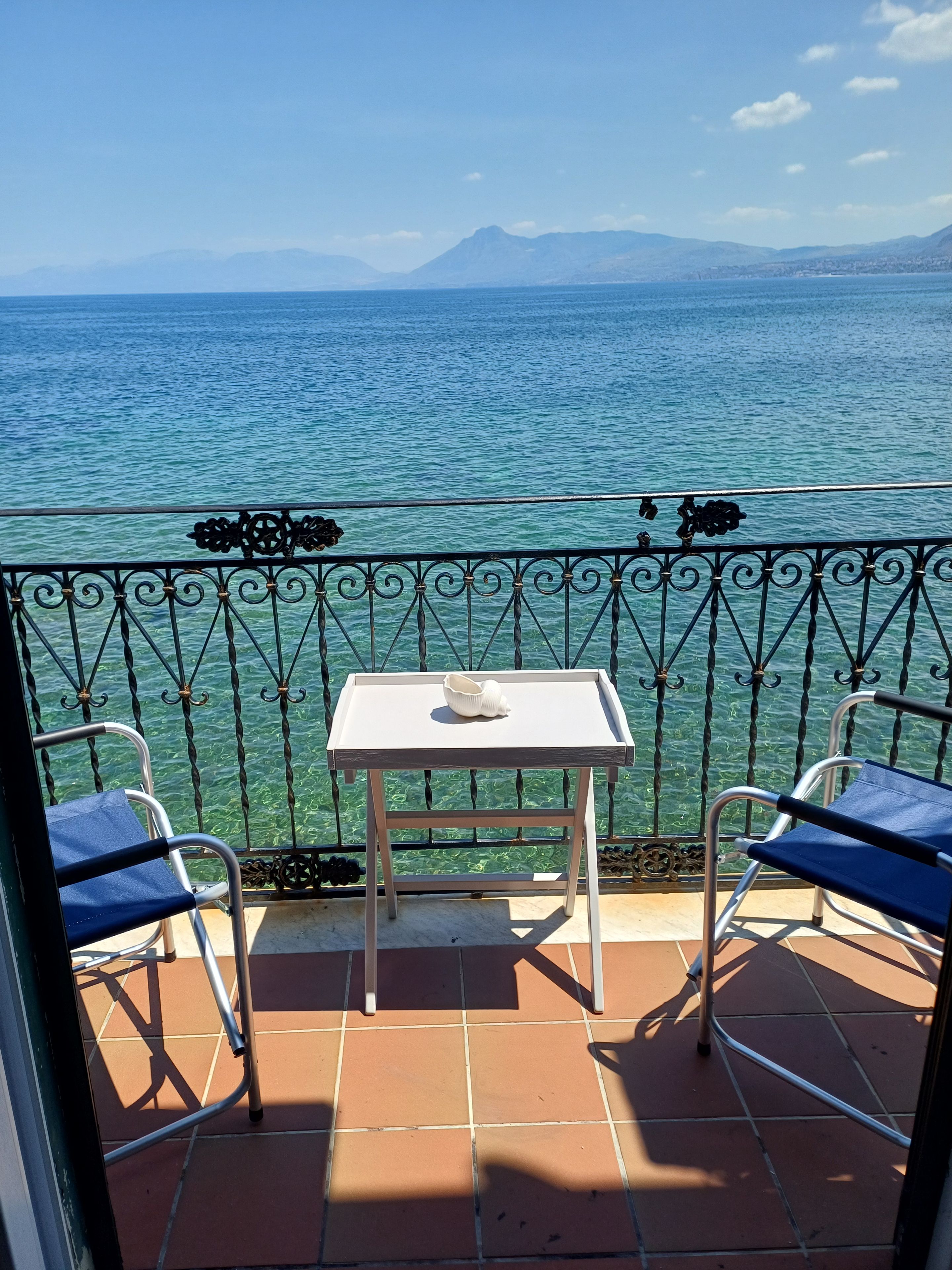 Un balcone con tavolo e due sedie, vista su un corpo d'acqua e montagne sullo sfondo.