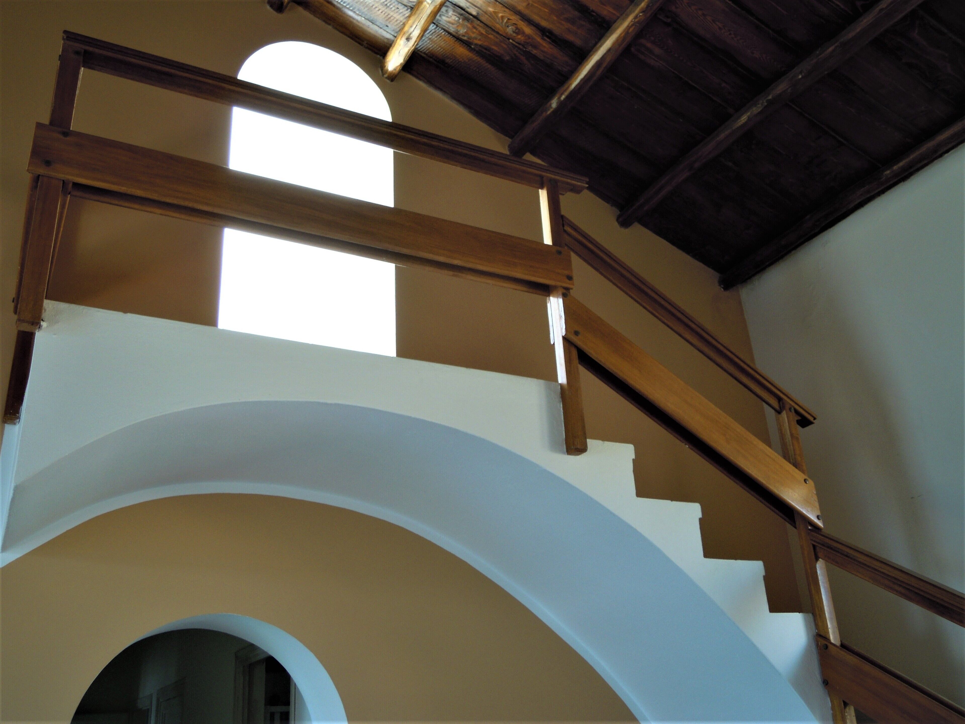 Una scala con ringhiere in legno e un arco bianco.