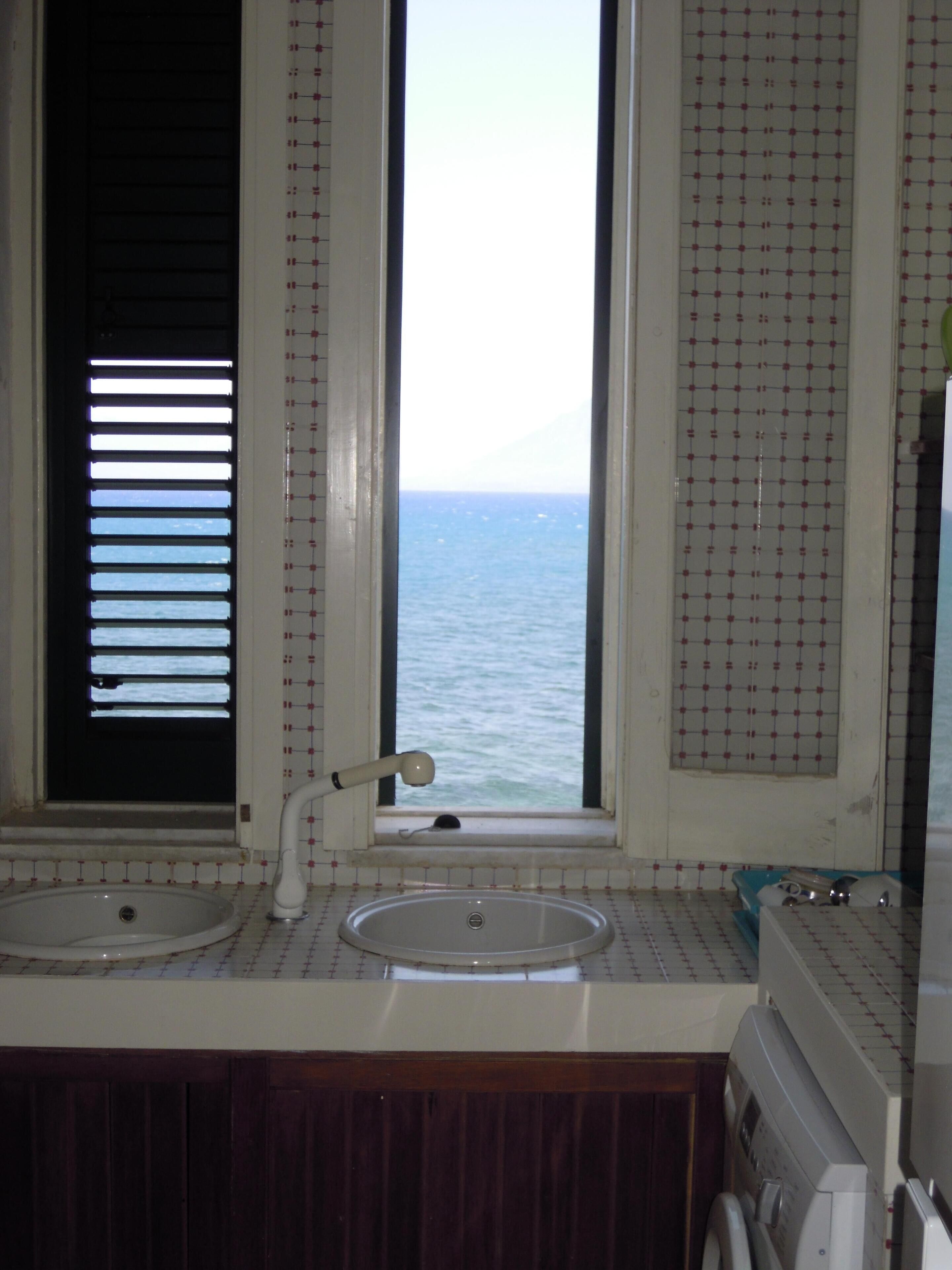 Un bagno con finestra vista mare, un lavandino e una lavatrice.