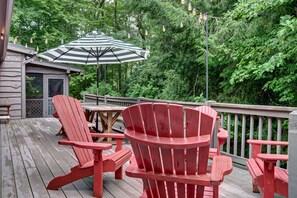 A wooden deck with red Adirondack chairs, a striped umbrella, and a wooden table. - Broadleaf Cottage in Mirror Lake Area of Highlands (Highlands)