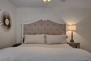 A bedroom with a tufted headboard, two pillows, a bedside table with a lamp, and a wall-mounted mirror. - Broadleaf Cottage in Mirror Lake Area of Highlands (Highlands)