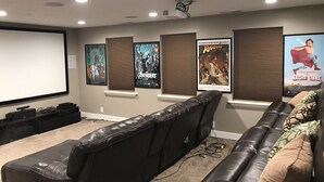 A home theater room with a large screen, a leather couch, and movie posters on the wall.