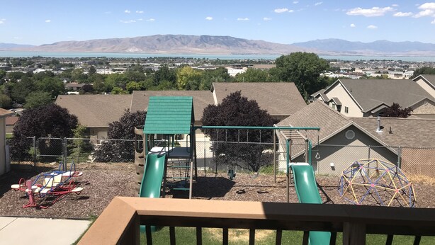 A playground with a slide and swings, surrounded by houses and a view of mountains and a lake.