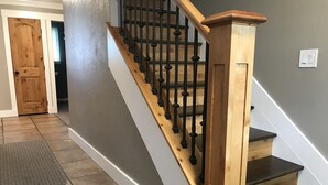 Eine Treppe mit Holzbalken und schwarzen Spindeln, die zu einer Zwischenebene mit einer Holztür führt.