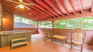 A covered patio with a hot tub, wooden rocking chairs, and a ceiling fan.