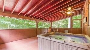 Un jacuzzi en una cabaña de madera con ventilador de techo, vigas de madera y ventanas grandes.