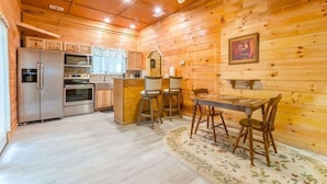 A wooden cabin interior with a kitchen, dining area, and a ceiling fan.