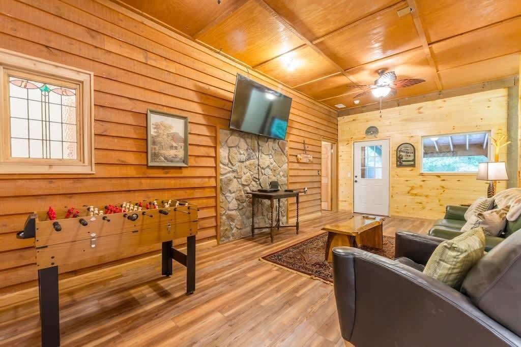 A cozy room with wooden walls, a stone fireplace, a foosball table, a television, and a sofa.