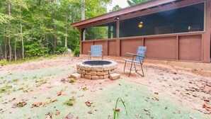 A cabin with a stone fire pit, two chairs, and a large window overlooking a forest.