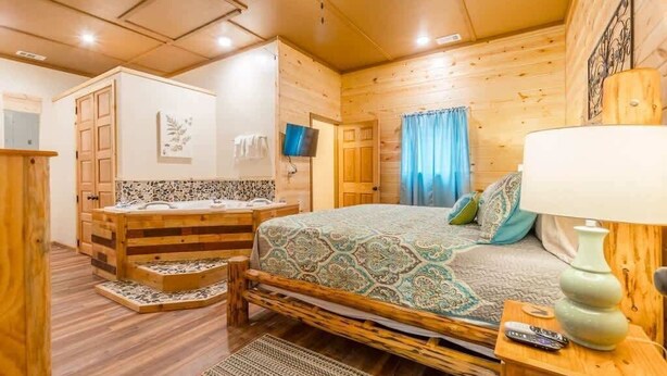 A wooden cabin bedroom with a bed, a wooden dresser, a TV, and a bathroom with a shower.