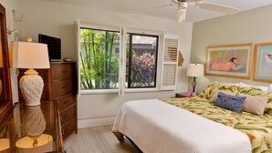 A bedroom with a bed, a dresser, a lamp, a window with blinds, and a ceiling fan.