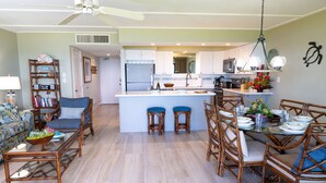 A spacious living area with a dining table set for four, a kitchen with modern appliances, and a ceiling fan.