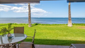 A patio with a glass table and chairs overlooking a grassy area and the sea.