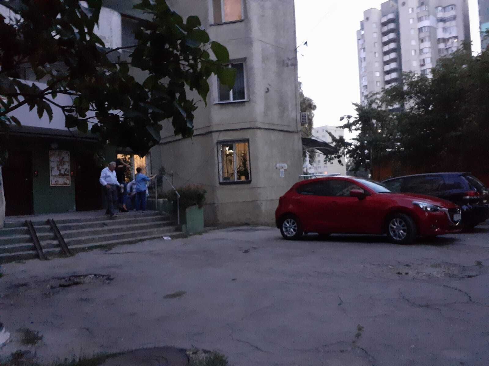 En bygning med en trappe, der fører op til en dør, en rød parkeret bil og et træ i forgrunden.