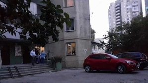 Un bâtiment avec un escalier menant à une porte, une voiture rouge garée et un arbre au premier plan.