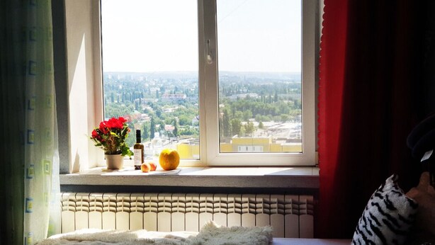 Une chambre avec une grande fenêtre, un radiateur en dessous, et une vue sur le paysage urbain.