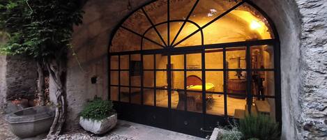 A stone archway entrance with a large window, a stone bench, and a planter with greenery.