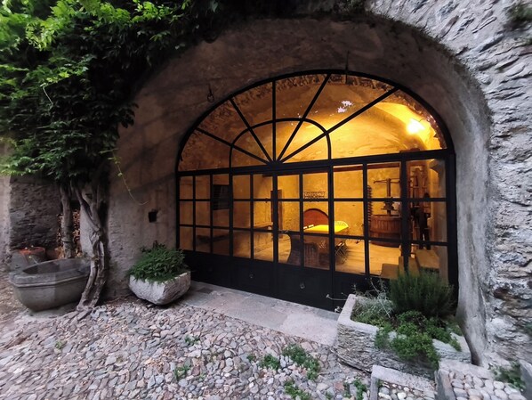 A stone archway entrance with a large window, a stone bench, and a planter with greenery.