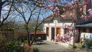 A rustic house with a brick facade, a tiled roof, and a garden with pink flowering trees.