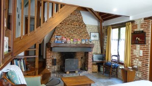 A cozy room with a brick fireplace, wooden staircase, and a television on a wooden stand.