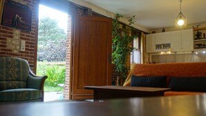 A cozy living room with a sofa, a chair, and a wooden table. There is a brick wall with a sign, a plant, and a view of the outdoors.