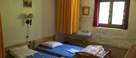 A small, simple room with two single beds, a sink, and a window with curtains.