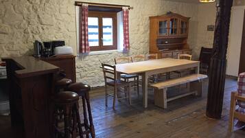 Een rustieke keuken met een houten tafel, barstoelen en een stenen muur.