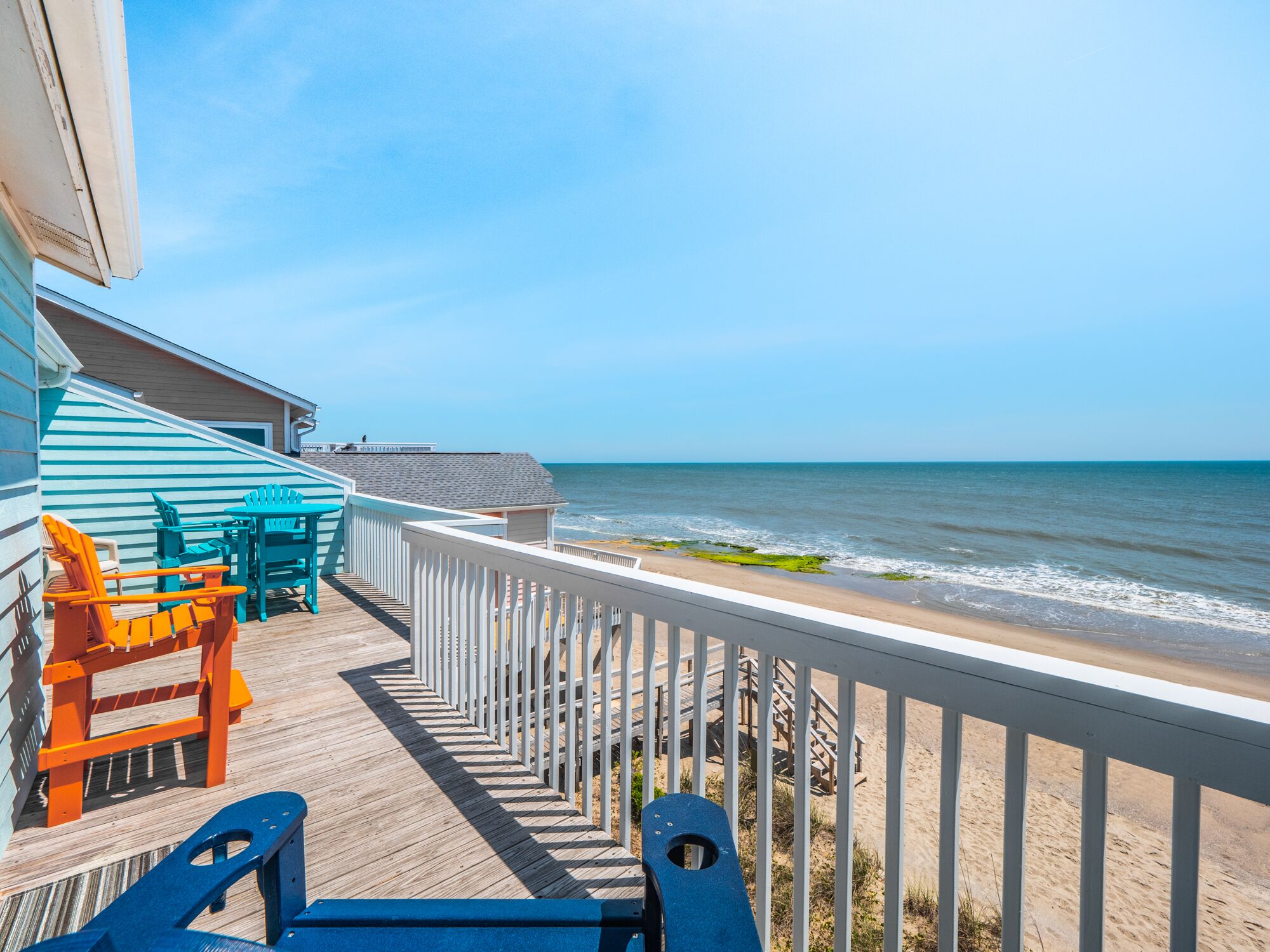 A wooden deck with chairs and a table overlooking a beach.