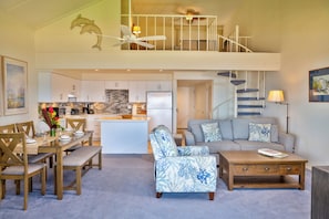 A spacious living area with a dining table, a sofa, and a coffee table. A kitchen is visible in the background with white cabinets and a refrigerator. - Maalaea Surf, Unit A5-2 Bedroom Beachfront Townhouse, AC, Wifi, TV, Kitchen (Kihei)