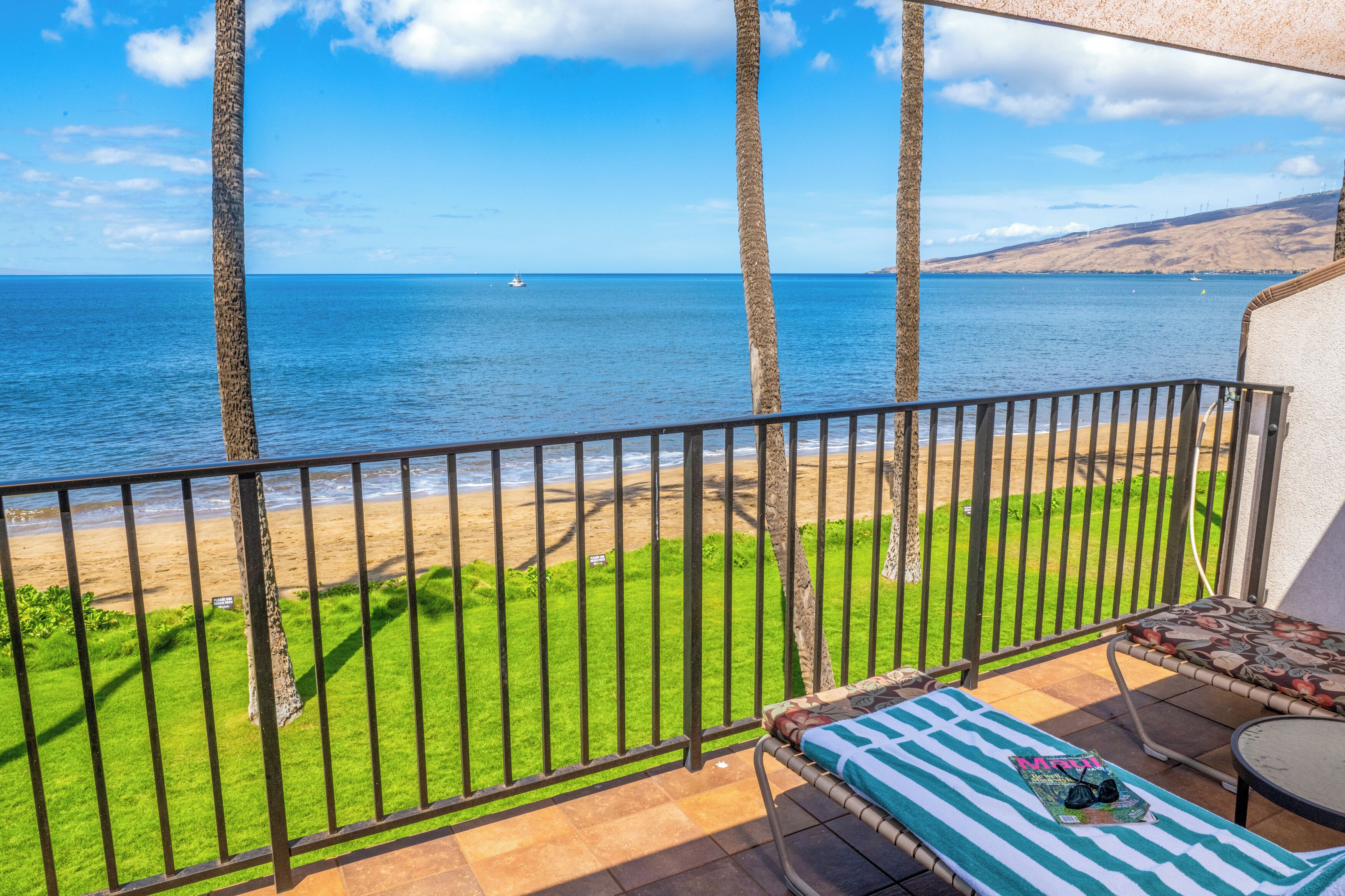 A balcony with a view of the beach and ocean, a lounge chair, and a small table.