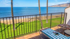 A balcony with a view of the beach and ocean, a lounge chair, and a small table. - Maalaea Surf, Unit A5-2 Bedroom Beachfront Townhouse, AC, Wifi, TV, Kitchen (Kihei)
