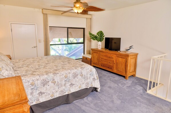 A bedroom with a bed, a wooden dresser, a television, and a plant.