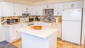 A modern kitchen with white cabinets, a central island, a microwave, a coffee maker, and a refrigerator. - Maalaea Surf, Unit A5-2 Bedroom Beachfront Townhouse, AC, Wifi, TV, Kitchen (Kihei)