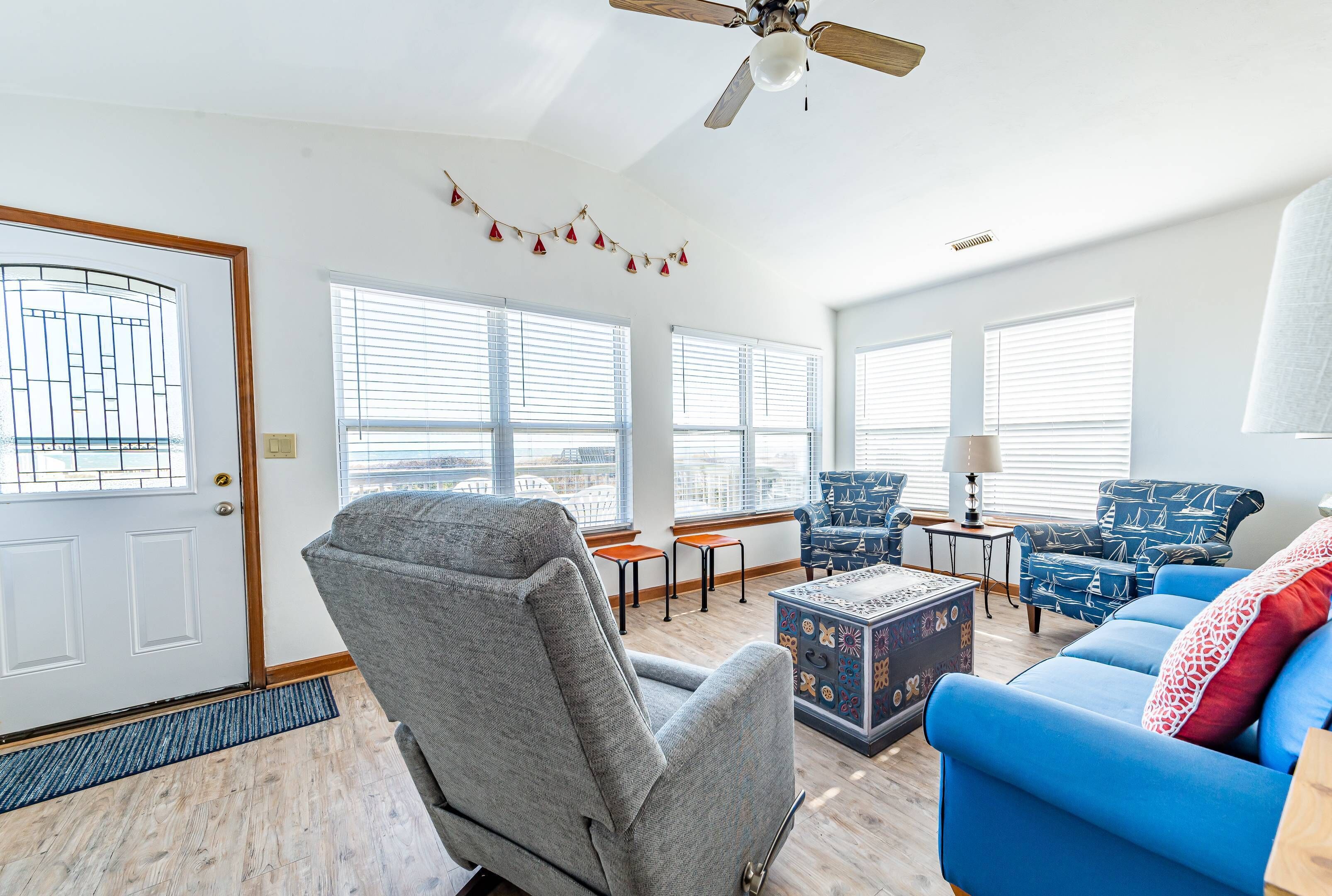 A spacious living room with a grey armchair, blue sofa, and patterned ottoman.