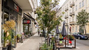 Una acera con mesas al aire libre, plantas en macetas y un café con un letrero.